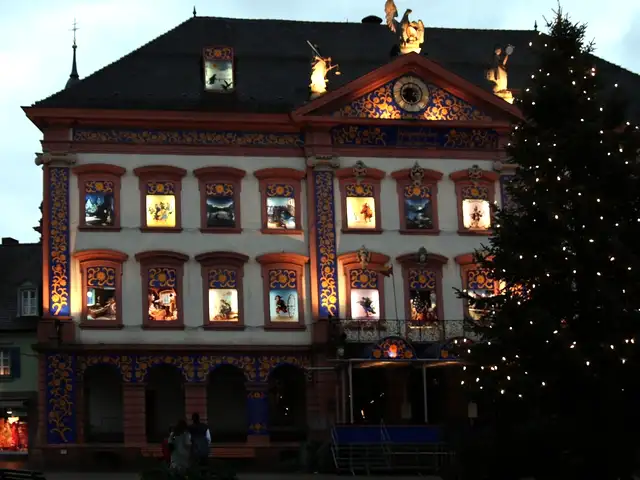 Historic town hall at dusk with brightly lit picture windows like opened advent calendar doors, a large lit Christmas tree beside it