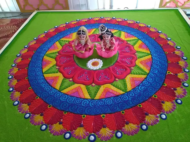 A large round rangoli in coloured powder on the floor, rings of red, blue, yellow and pink petals around a flower centre