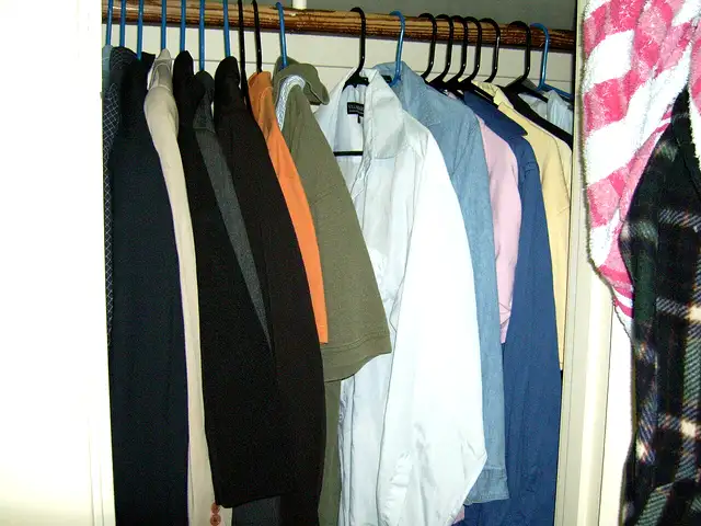A home closet rail packed tight with shirts and jackets on mismatched hangers, a striped towel squeezed in at the end