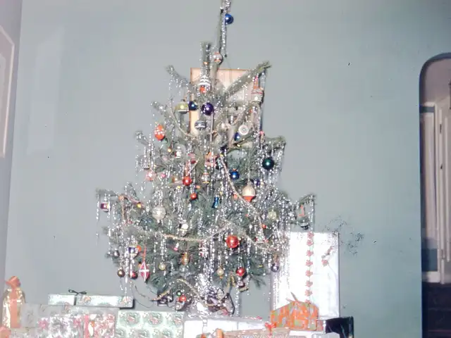 Decorated Christmas tree with tinsel and wrapped gifts beneath it in a mid-century living room