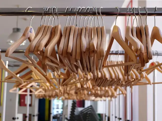 Rows of empty wooden clothes hangers on metal garment rails in a shop, with blurred colour panels behind