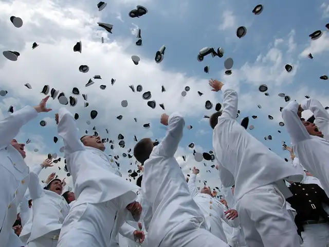 Graduation caps thrown high into a blue sky over a crowd of graduates in white, photographed from below