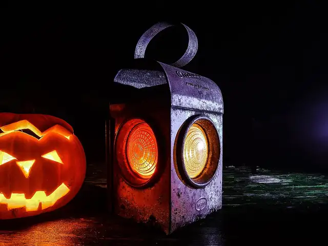 A carved jack-o'-lantern glowing beside a lit vintage railroad lantern on a wooden surface