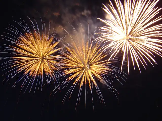 Three golden fireworks bursting at once against a dark night sky
