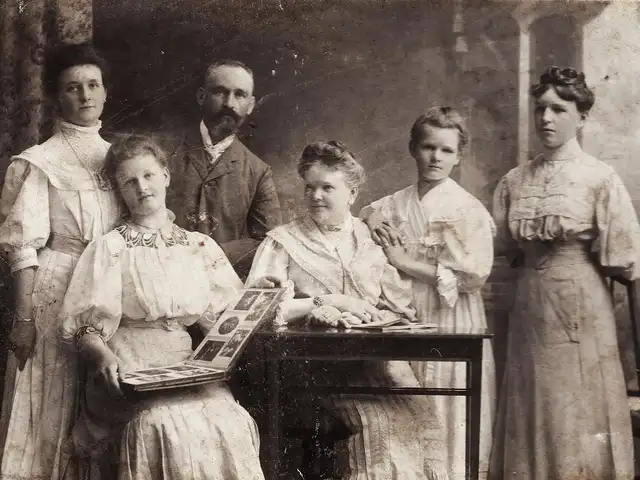 Edwardian-era family portrait in a photography studio, one of the women holding an open photograph album